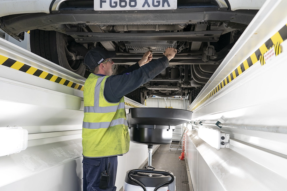 A technician inspecting the underside of a lorry from the workshop pit